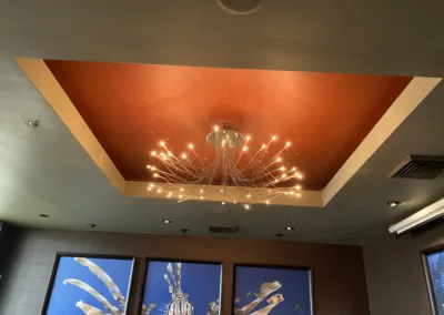 The ceiling of a restaurant is decorated with paintings and a chandelier.